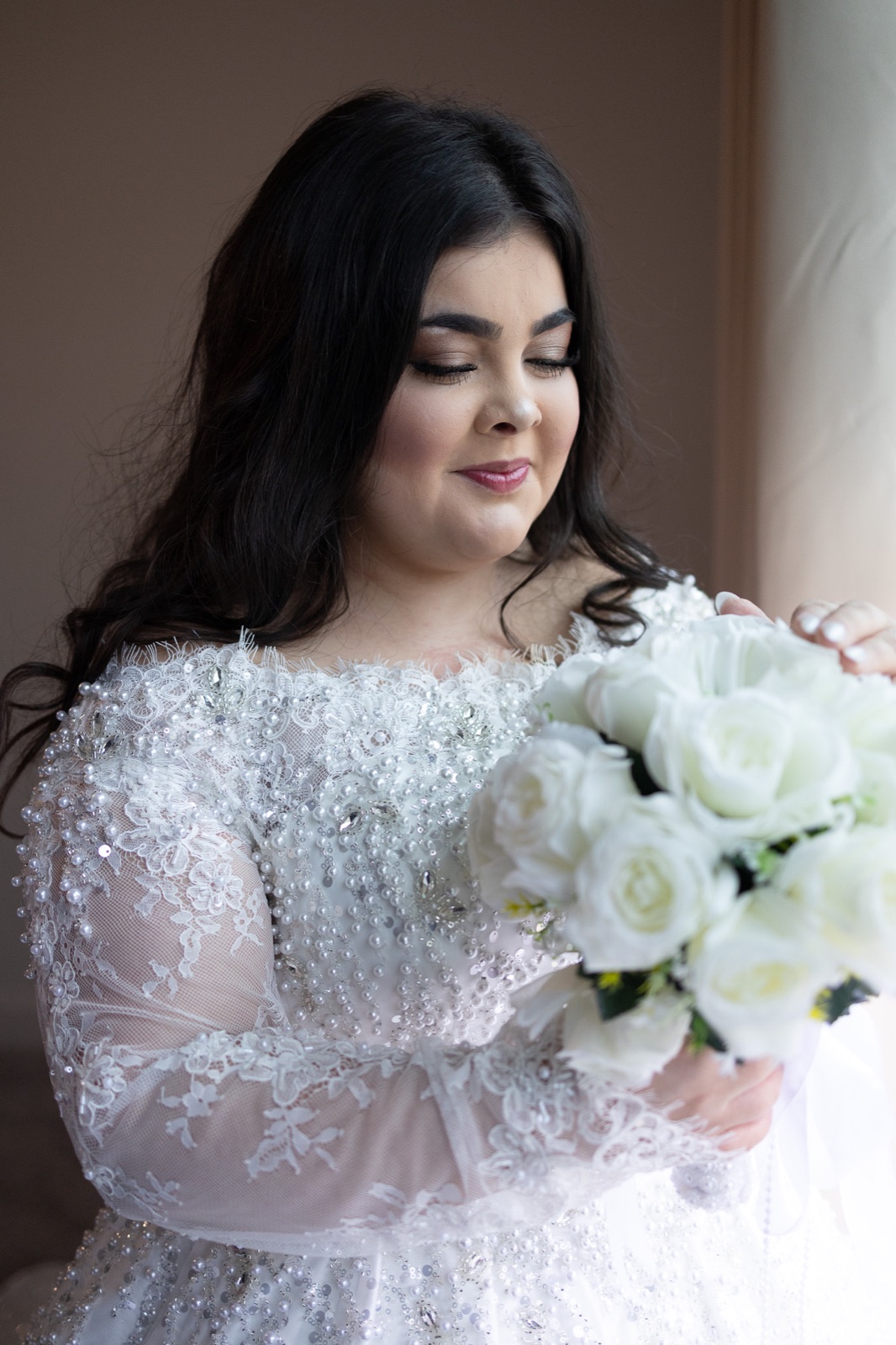 Bride looking down at her white rose bouquet by the window