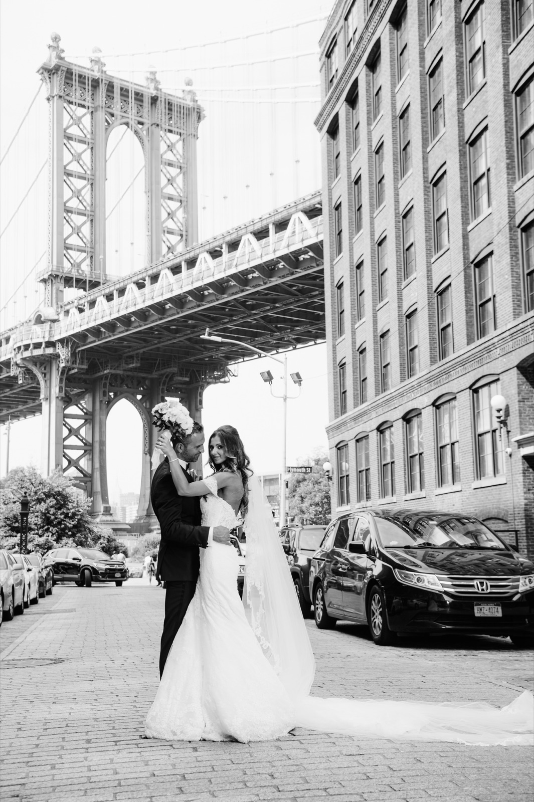 Black and white photo of the couple under the Manhattan Bridge in DUMBO